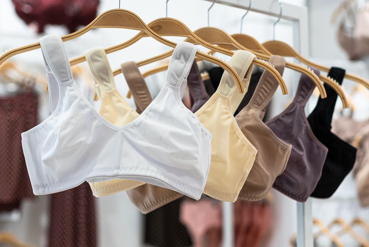 Close-up of sports bras in various colors displayed on wooden hangers in a fashion store.